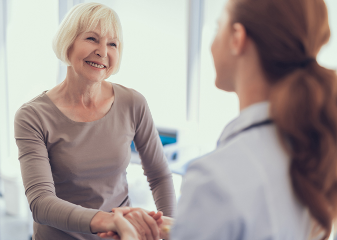 Senior woman and healthcare worker grasp hands in a friendly greeting.