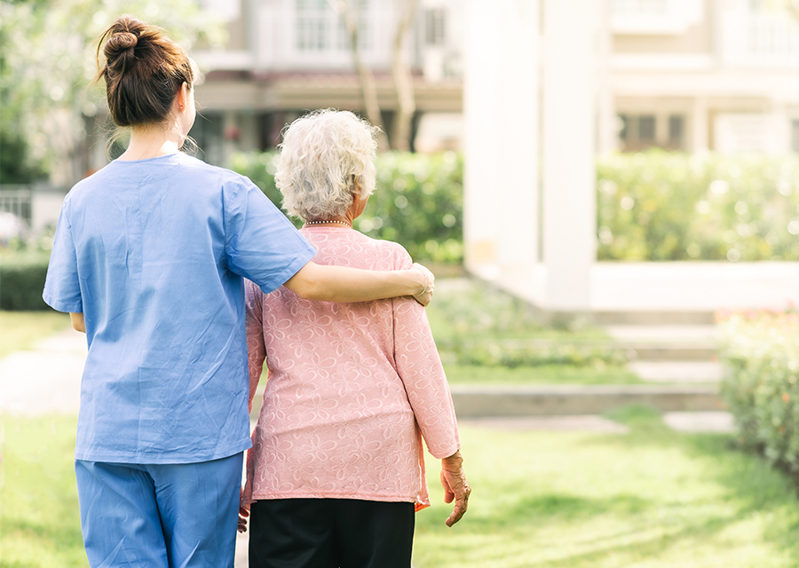 Nursing assistant guides a senior client in an outside walk