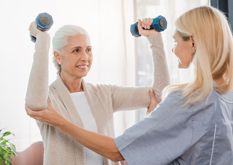 Senior exercises with hand weights, assisted by a physical therapist