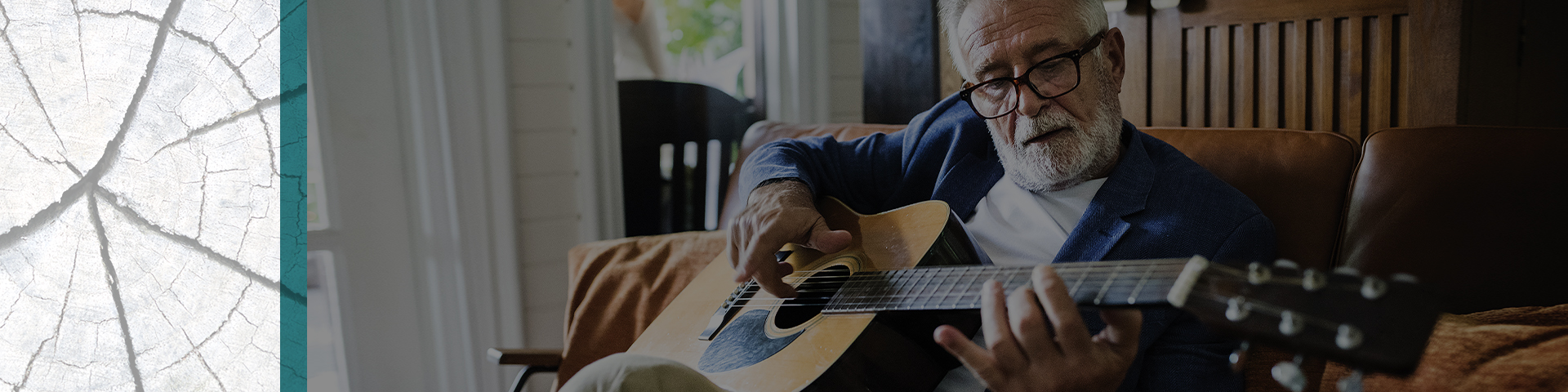 Smartly dressed bearded senior plays guitar on a couch.