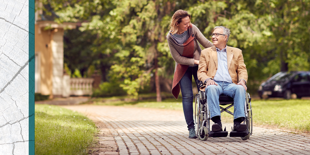 Adult child pushes senior father in a wheelchair down a cobbled pathway